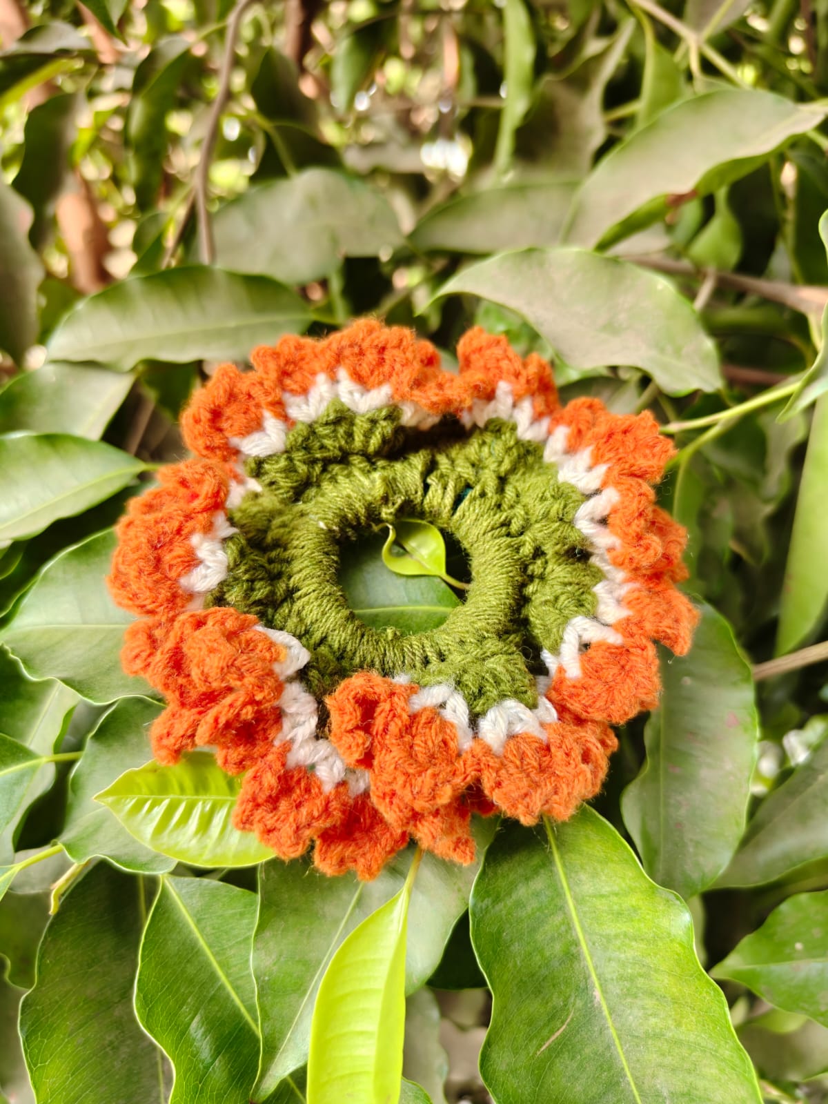 Bright crochet sunflower and daisy arrangement in a woven basket with green leaf accents.
